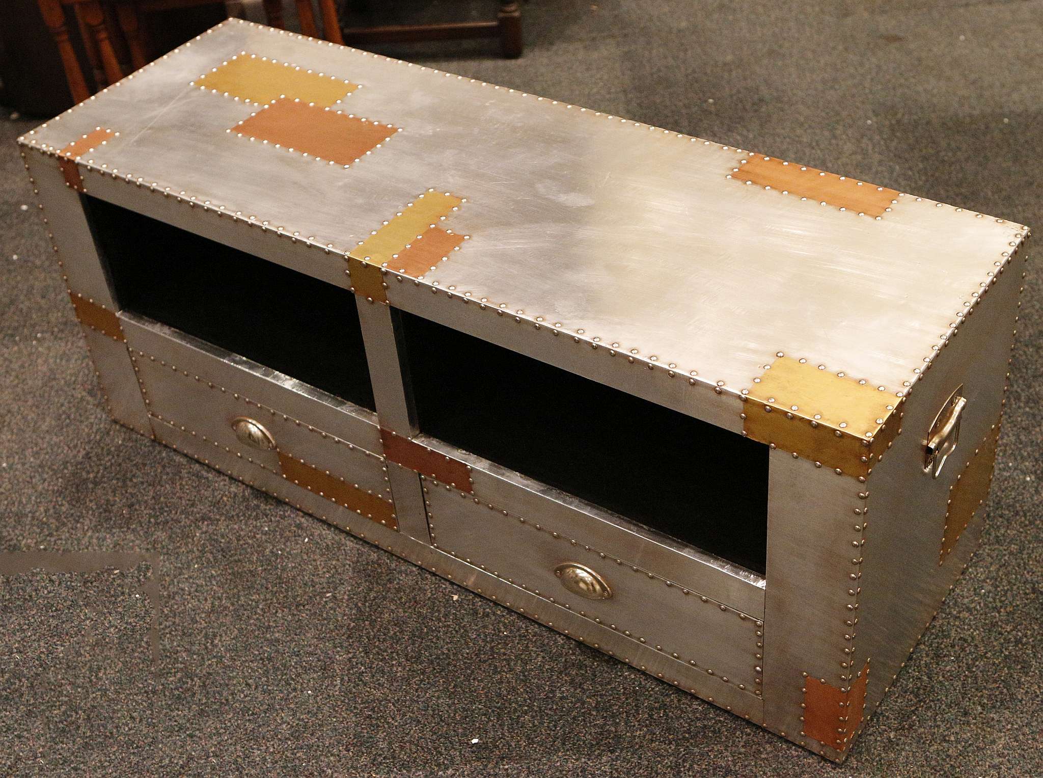 A riveted aluminium and copper patchwork television stand with two drawers and two storage openings,