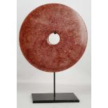 A red variegated composite marble disc and stand, 29cm diameter.