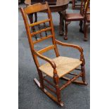 A mahogany rocking chair with spindle decorated back rest over a rush seat, flanked by open arms, on