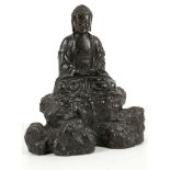 A Sino Tibetan figure of a Buddha, seated with hands together and legs folded beneath, on a rocky