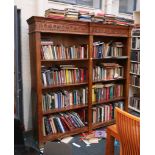 A 20th century, double front set of open bookcases in tropical hardwood and having a carved top