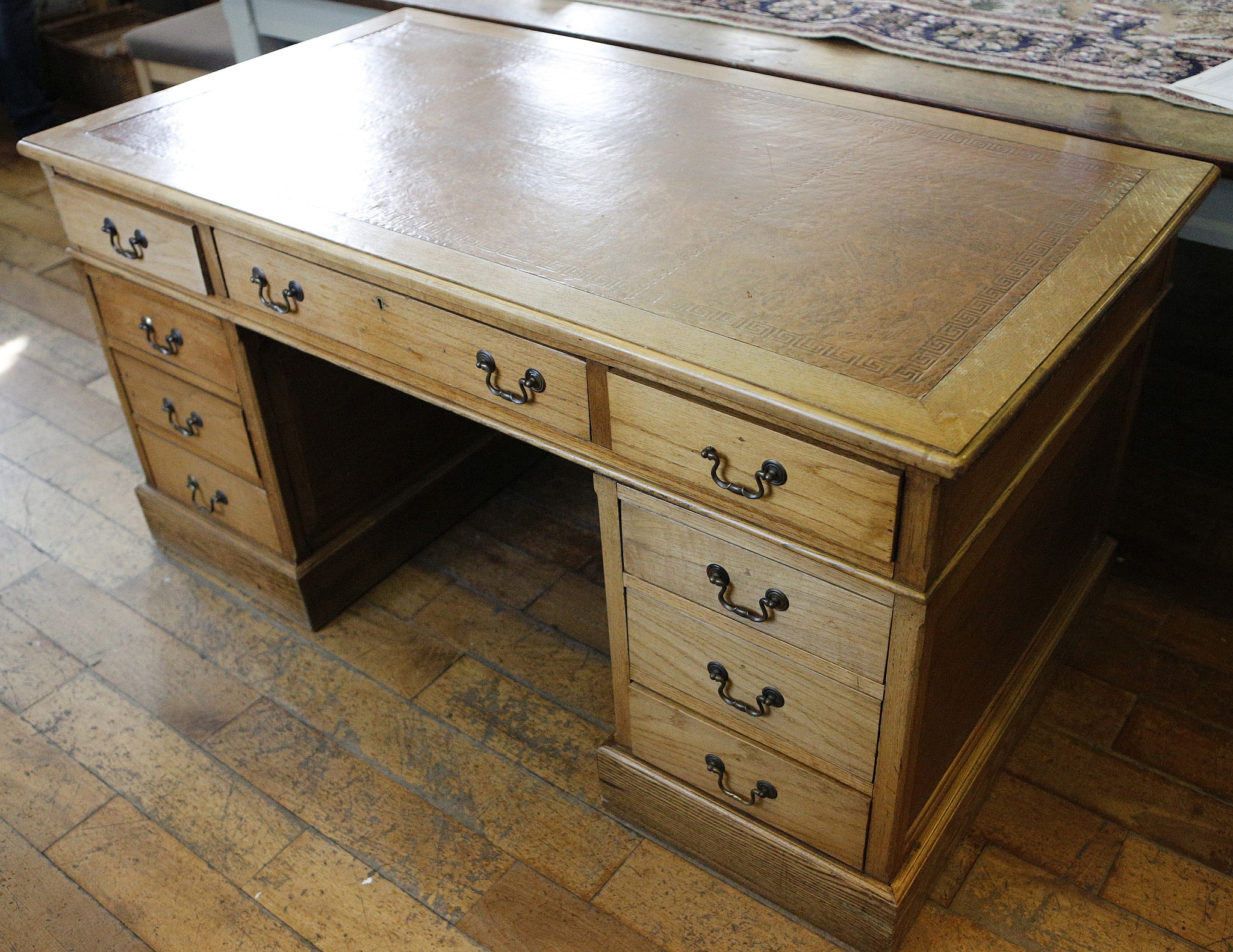 A light oak twin pedestal desk, brown leather insert, Greek key tooling,m 9 drawers, bronzed swan