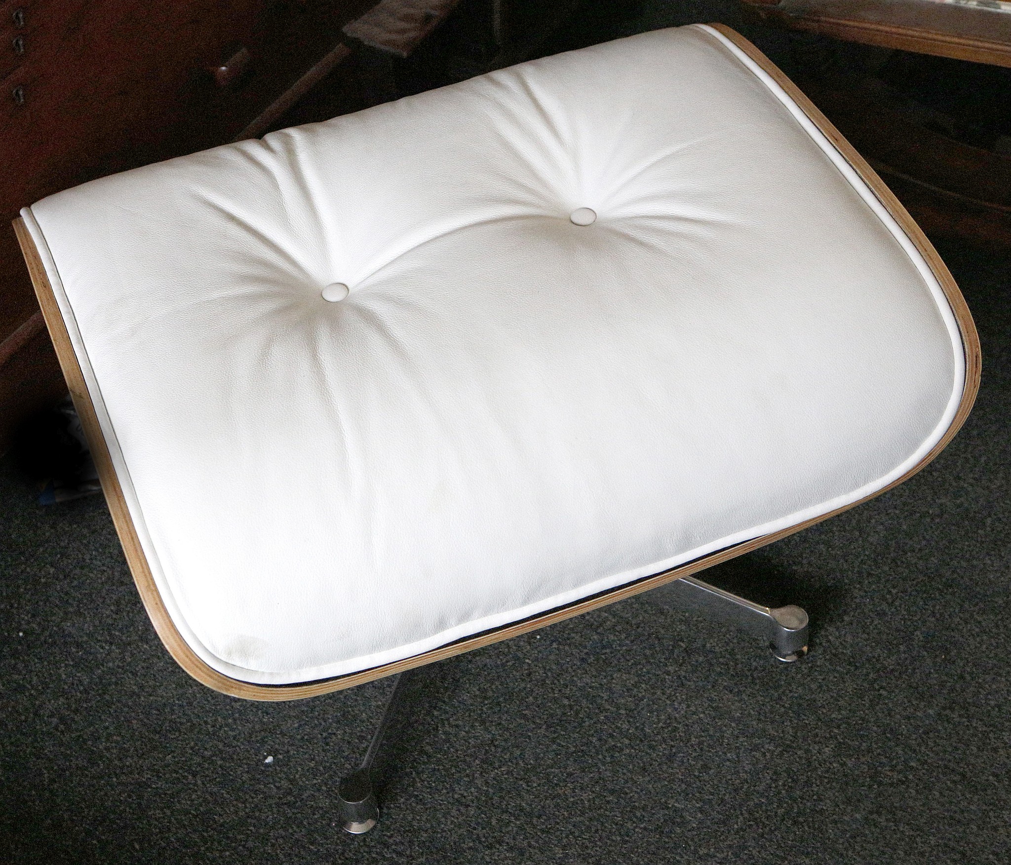 An Eames inspired ottoman, having white faux leather upholstery, raised on chrome base, 41 H x 65