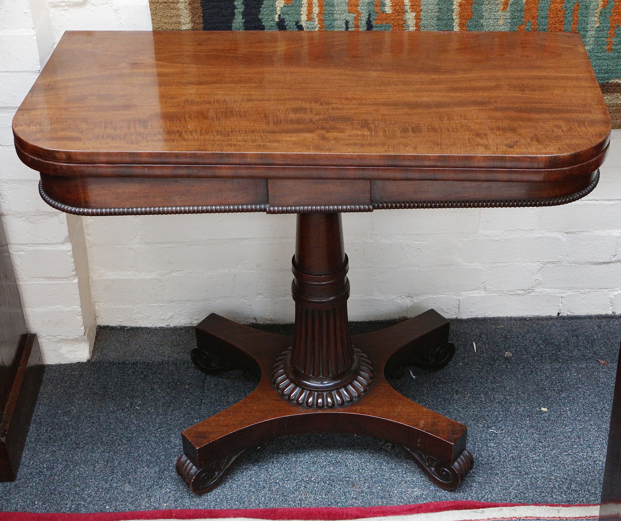 A Victorian mahogany card table, with 'D' shaped top, raised on fluted column support and platform