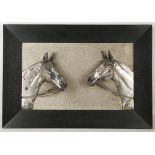 A white metal bass relief picture of two horses heads, together with another similar.