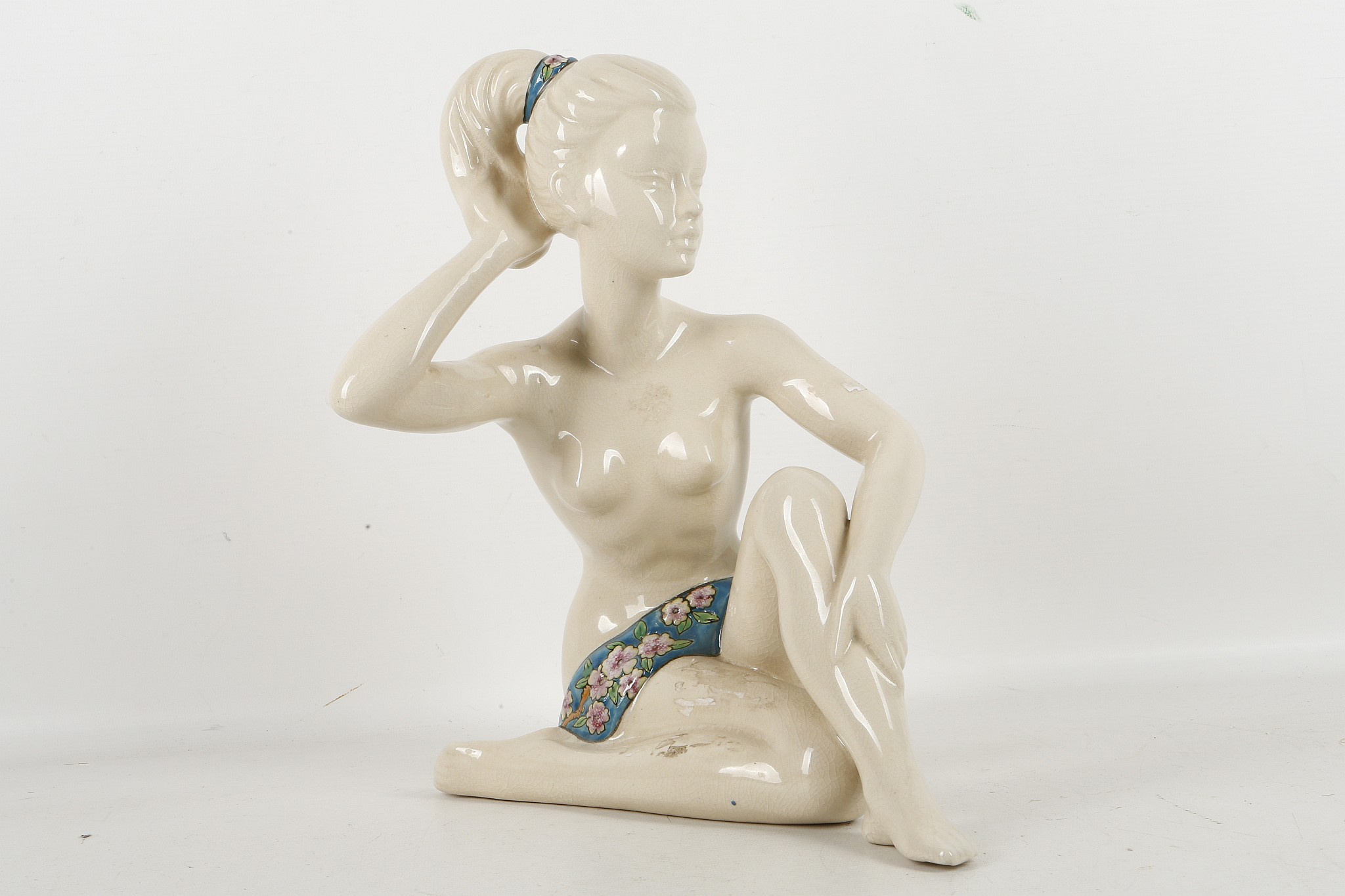 A French porcelain figure of a nude girl kneeling with enamelled drape and headband.