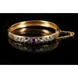 A Victorian high carat gold hinged bangle, set with an oval faceted amethyst flanked by diamond