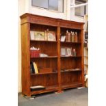 A 20th century, double front set of open bookcases in tropical hardwood and having a carved top