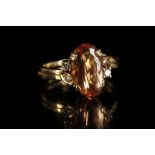 A yellow metal, peach topaz, and diamond ring, set oval cut topaz flanked by four round cut diamonds