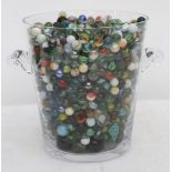 A quantity of marbles contained in a large glass ice pail.