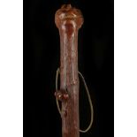 A FOLK ART NATURAL 'TEXTURED' WOOD STICK. The knop carved as a pig nosed man with glass eyes over