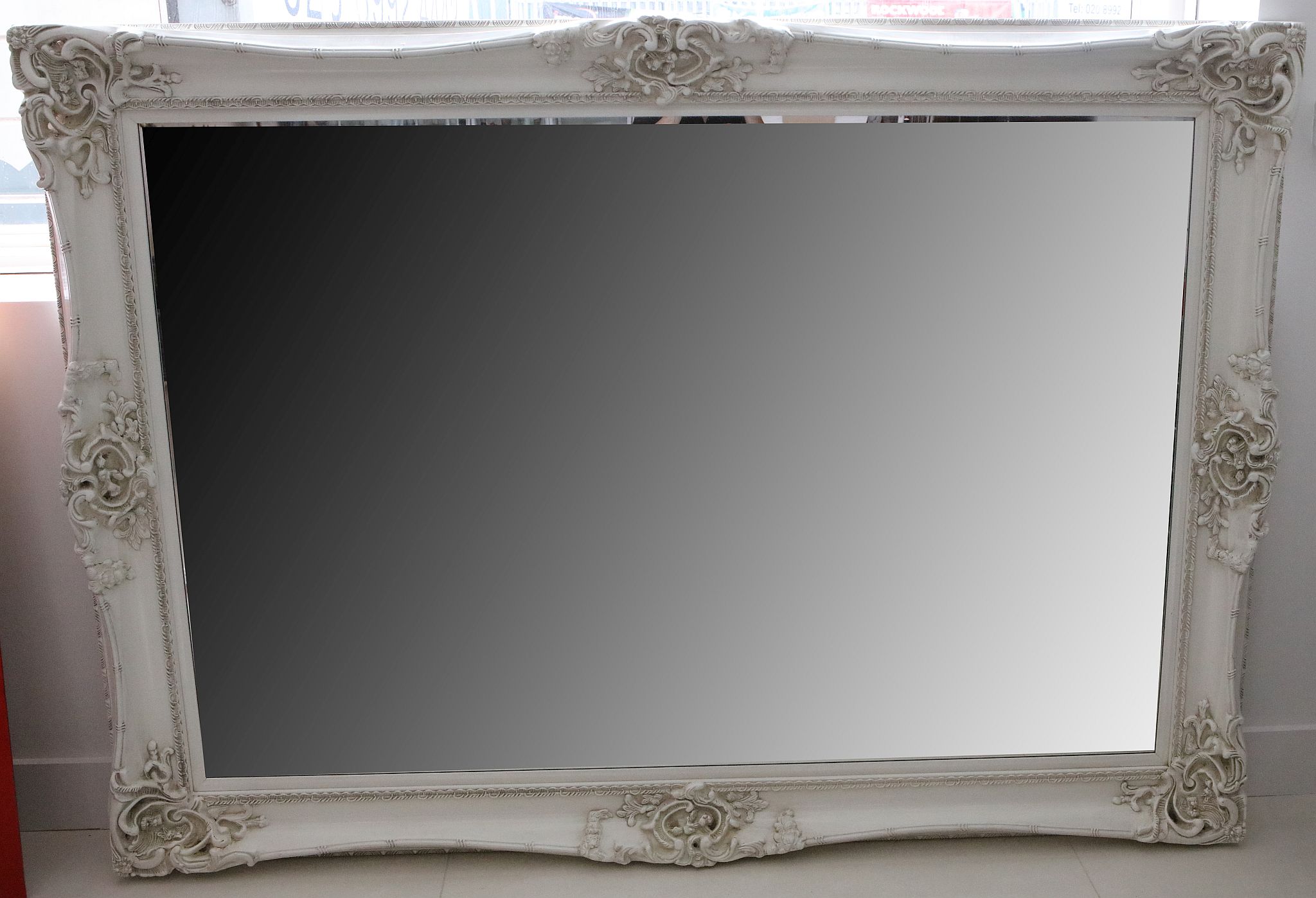 A large modern mirror, with ornate white painted carved wooden frame, 215 x 103cm.