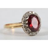 An 18 carat yellow gold, diamond, and garnet cluster ring, set oval garnet surrounded by diamond