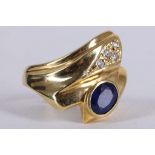 A 14 carat yellow gold, sapphire, and diamond crossover style ring, having bezel set blue