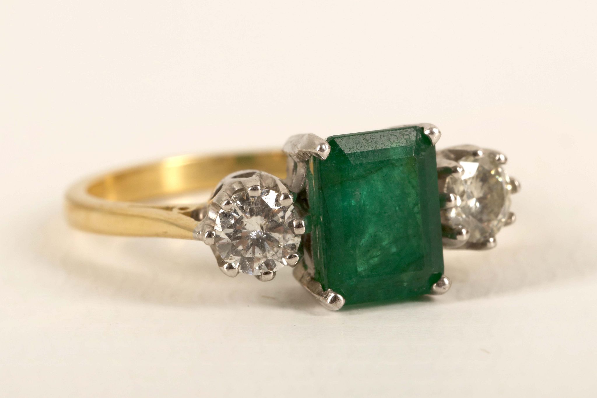 An 18ct gold, emerald and diamond three stone ring, the emerald cut main stone flanked by