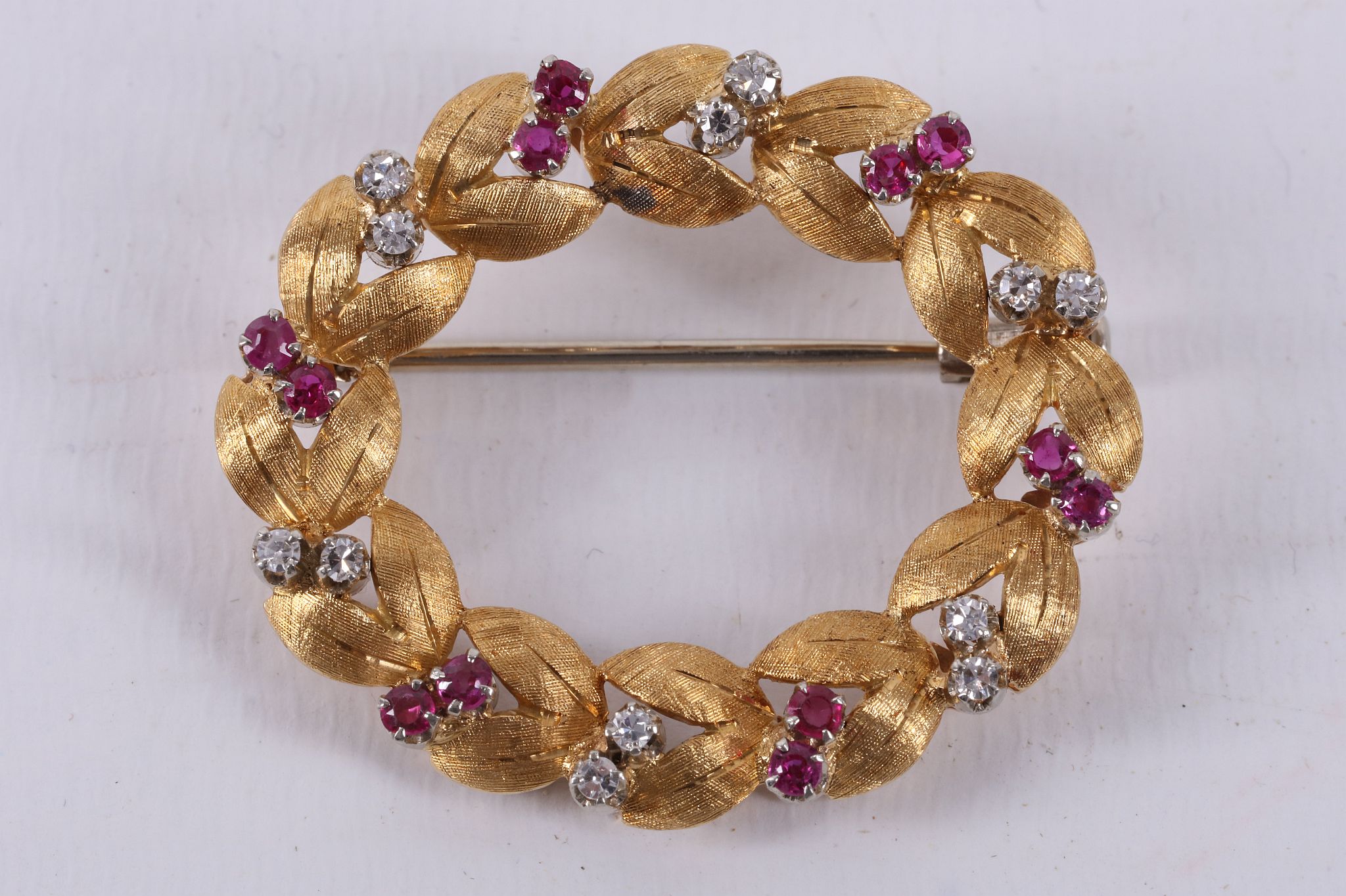 An 18ct gold foliate wreath brooch, the leaves interspersed with claw set diamond and ruby pairs.