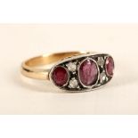 An antique gold, ruby and diamond set curved panel ring, the three graduated oval faceted cut rubies