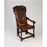 A late 17th Century fruitwood and elm panel back armchair, with scroll and leaf cresting above a