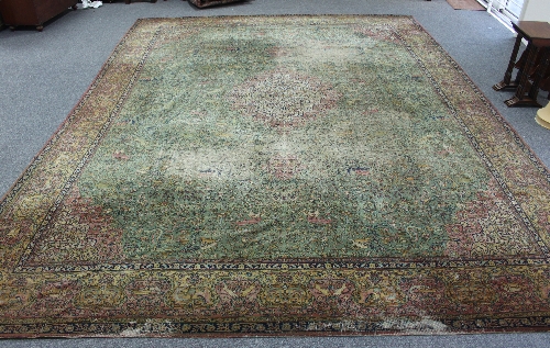 A large Persian rug worked with forest scenes on a green border with central red medallion within