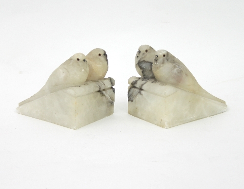 A pair of Art Deco alabaster book ends, each carved with a pair of budgerigars on a sloping ledge,