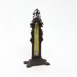 A Victorian gothic thermometer with brass scale in a metal frame applied grotesque figures etc,