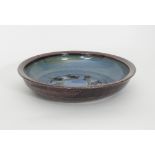 Russell Collins/A stoneware circular platter decorated in blue on a black ground with wax resist,