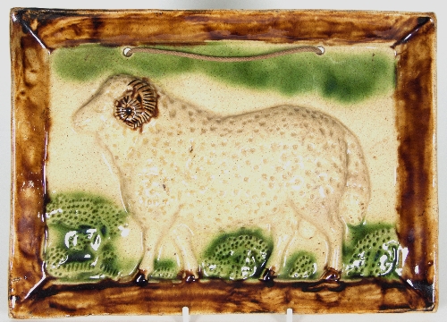 A Scottish lead-glazed earthenware plaque, moulded in relief with a ram in a pastoral setting,