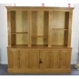 A large pine bookcase, the top section of three open shelves above three pairs of panelled doors,