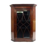 An early 19th Century oak corner cupboard, with moulded cornice enclosed by a glazed bar door,