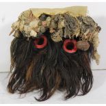 Wee Peoples, Nigeria Ngere dance mask covered with hair, fabric, and bells surrounding the red eyes,