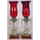 Pair of hurricane candle lusters, now as electrified lamps, the cranberry glass etched shades