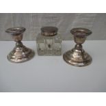 A pair of sterling silver pigmy candlesticks and a silver topped ink bottle