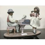 A Lladro china figure modelled as a Young Girl and Boy singing and playing the piano (girl's hair