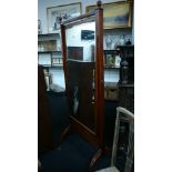 A large mahogany inlaid cheval mirror with finials to top resting on brass castors.