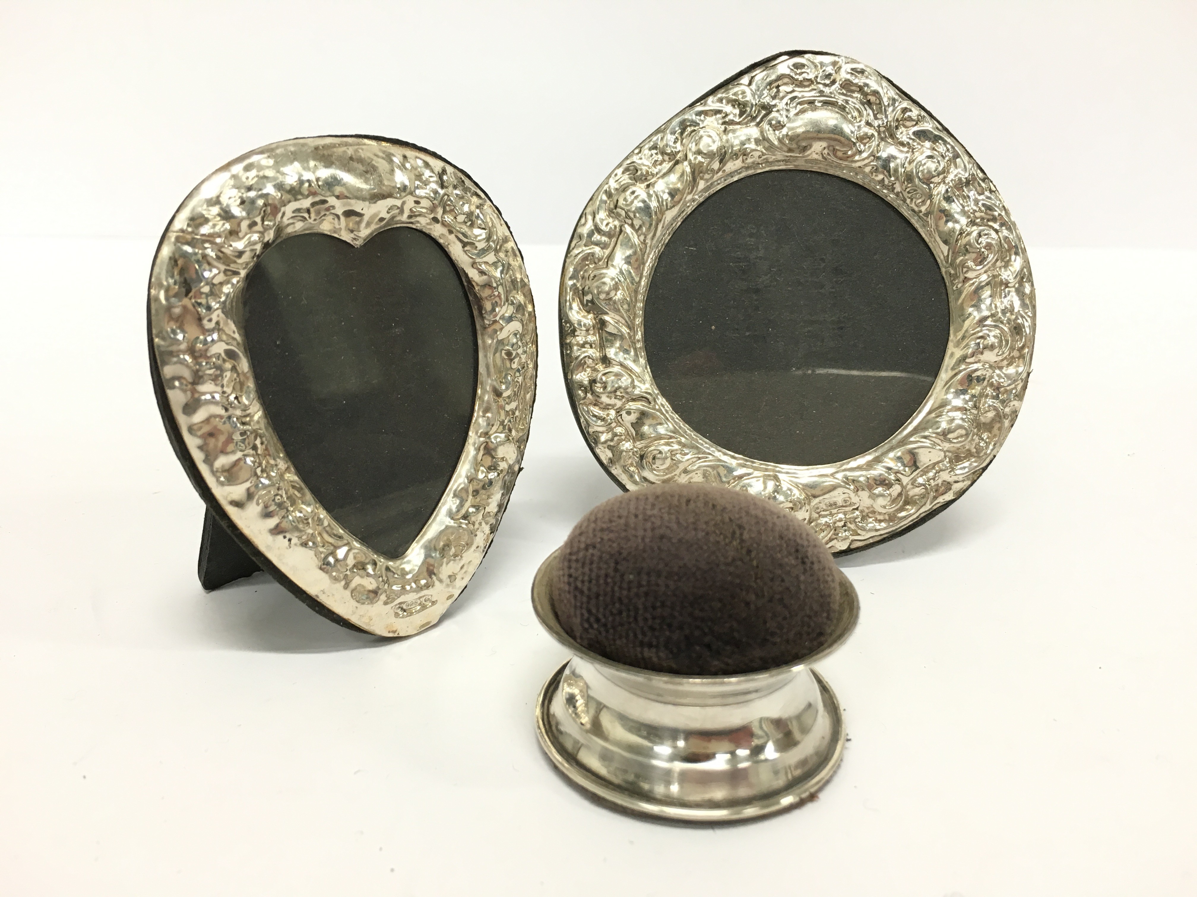 A small heart shaped silver photograph frame together with another and a silver pin cushion.