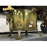 A large brass log basket with lion mask ring handles.