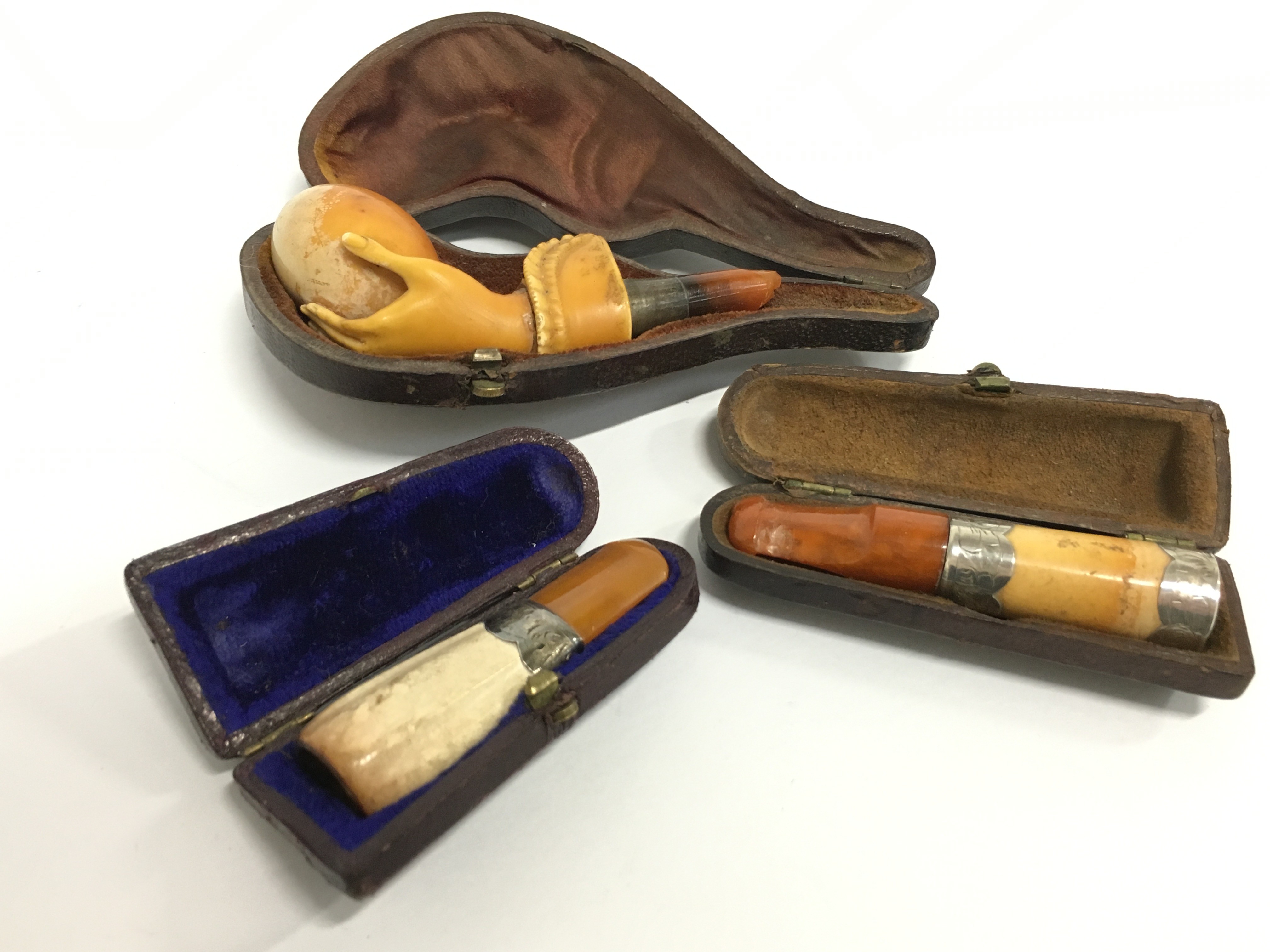 A 19th century Meerschaum pipe modelled as a hand holding an egg (af) together with two amber and