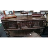 A large oak buffet with heavily carved doors to front and under tier resting on cup and cover