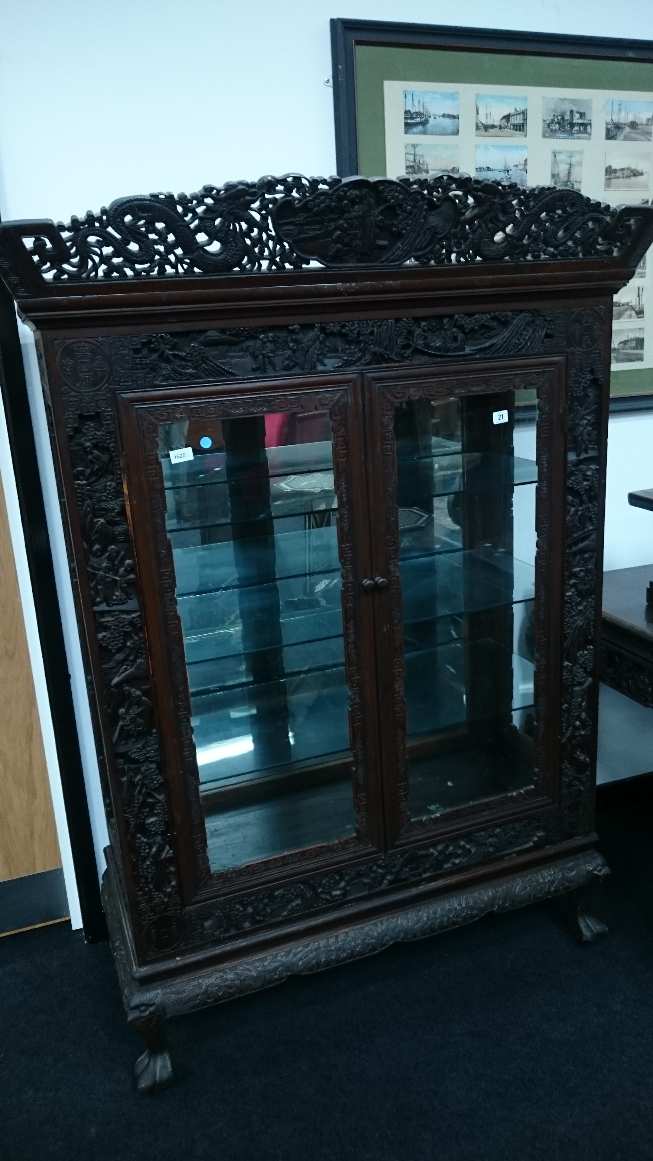 A large glazed two door display cabinet in the Chinese style with heavily carved top frieze and