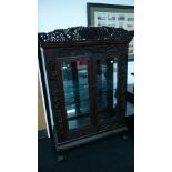 A large glazed two door display cabinet in the Chinese style with heavily carved top frieze and