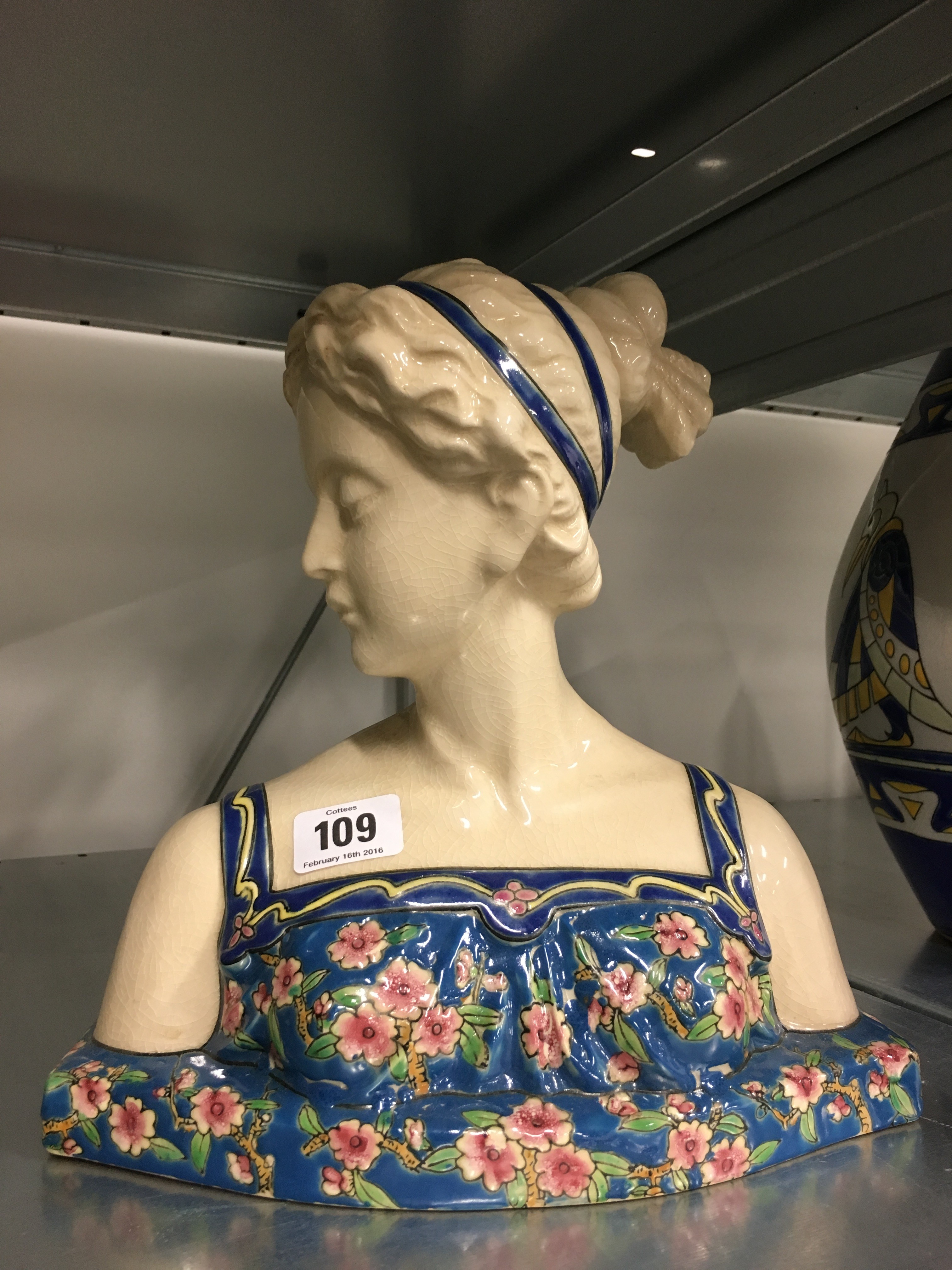 A Longwy style china bust modelled as a young girl wearing a floral strap dress.