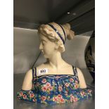 A Longwy style china bust modelled as a young girl wearing a floral strap dress.