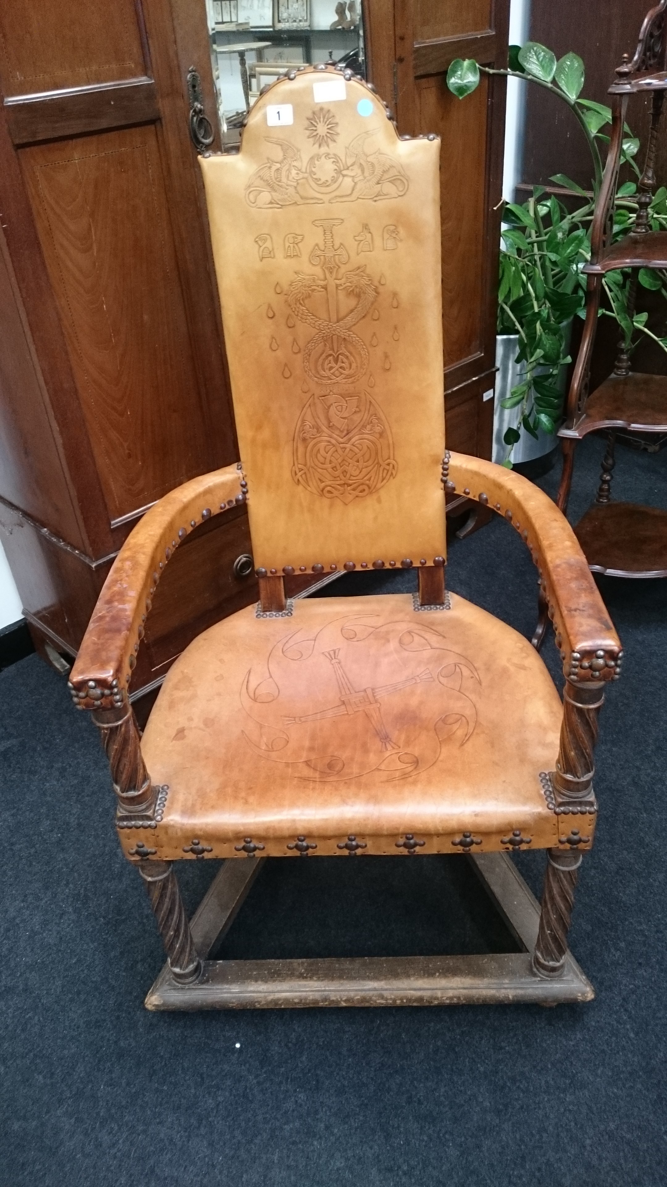 An Arts and Crafts style tooled leather ceremonial chair with open arms,