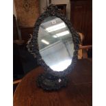 A Victorian gesso black painted ladies dressing table mirror, resting on a floral shaped base.