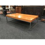 A low coffee table with wooden top and stainless steel supports in the style of Merrow Associates.