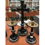 Three mid 20th century black painted altar pieces comprising a crucifix and pair of candlesticks