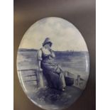 A Doulton Burslem blue and white oval plaque depicting a Dutch girl sitting on a breakwater,