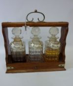 Edwardian oak three bottle tantalus with sliding drawer action,