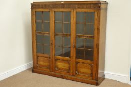 Early 20th century medium oak bookcase enclosed by three glazed doors, fluted and carved detail,