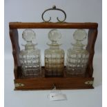 Edwardian oak three bottle tantalus with sliding drawer action,